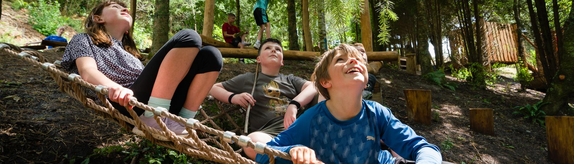 Children lying in a net in a wooded play area