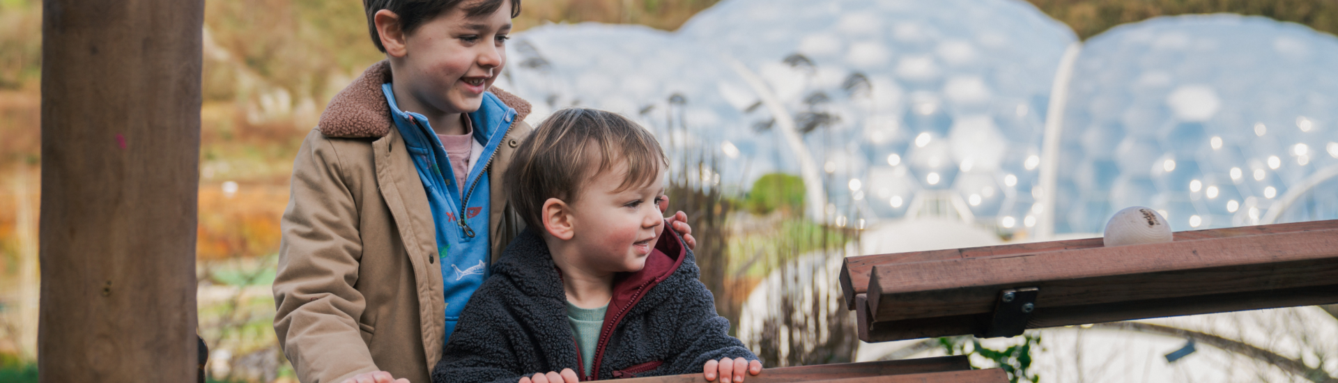 Two brothers playing on the wooden marble run with the Biomes in the background