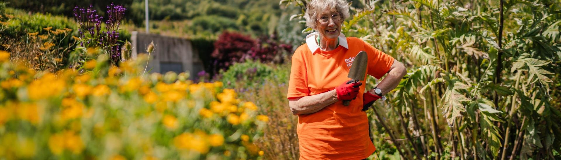 Eden Project volunteer holding a trowel and wearing a bright orange t-shirt