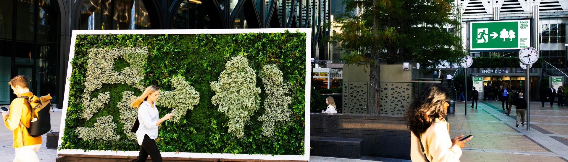 Three people walking in front of plant screen with an exit sign into nature