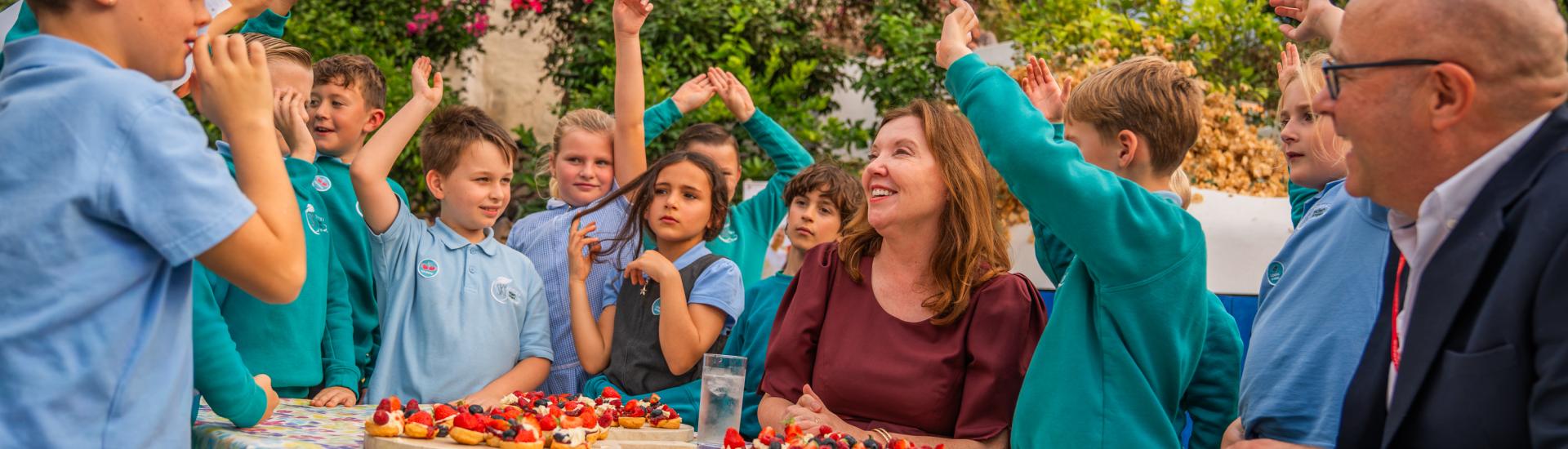 Children gathered round the Children's Commissioner, Rachel de Souza and Eden Project CEO at a table with scones