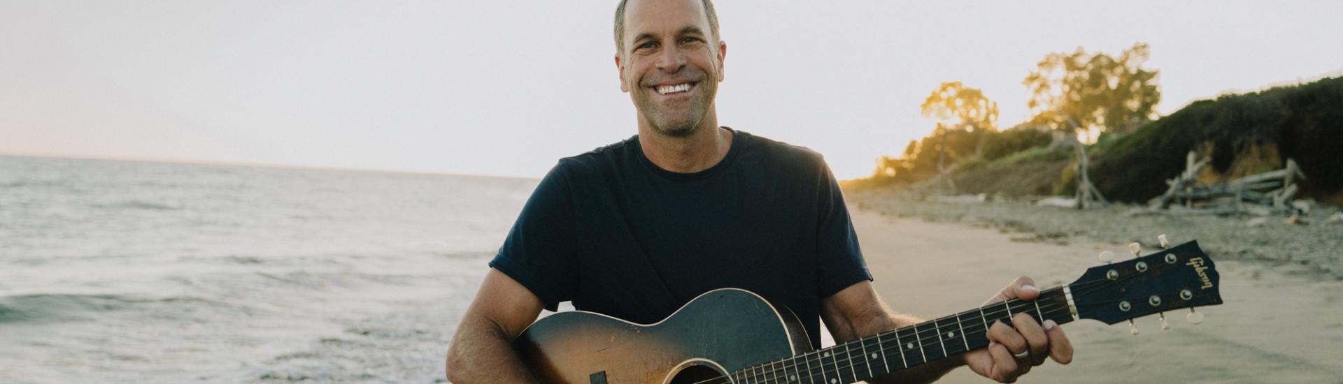 Jack Johnson with his guitar on a beach