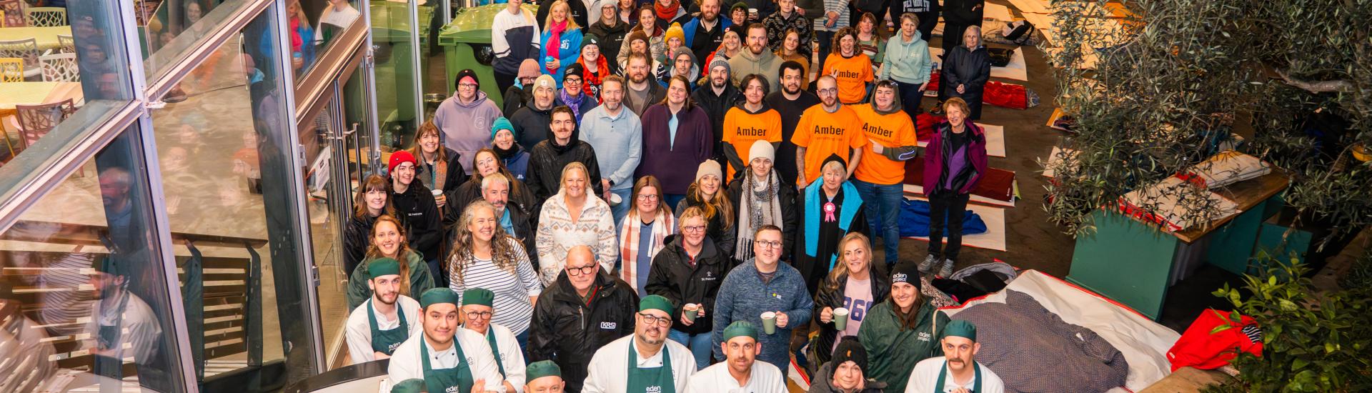 Group of Sleep Out attendees stood together outside the Link Building with a sign that reads SLEEP OUT